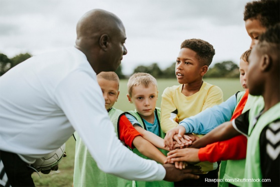 Stock photo of an adult clasping hands with a group of young boys on a playing field