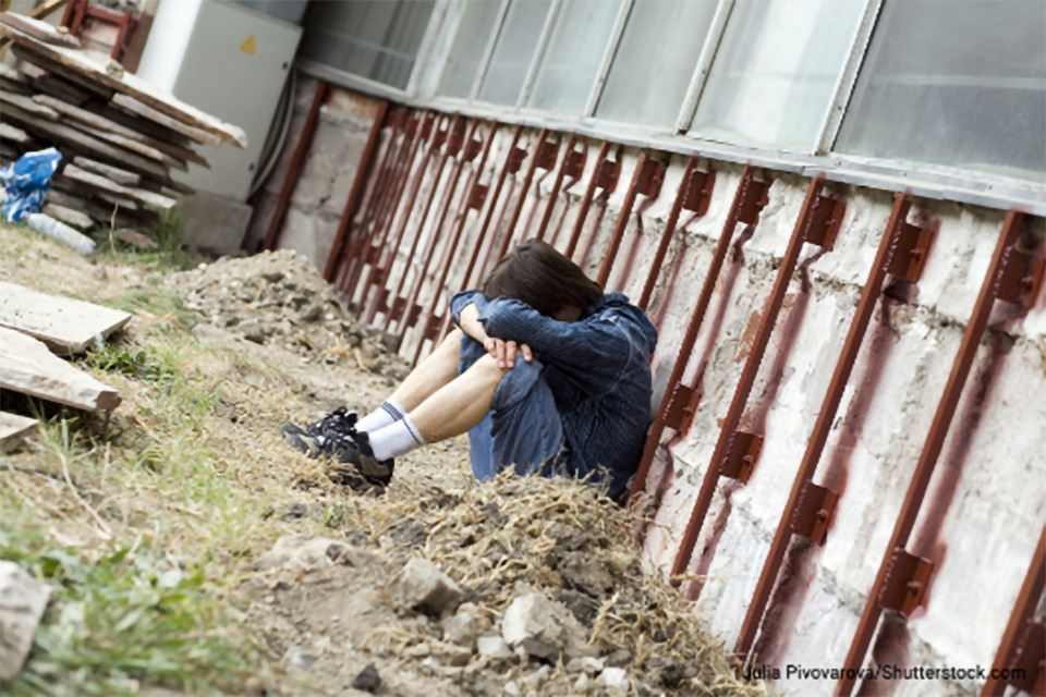 Stock photo of a young male sitting outdoors with his head resting on his knees