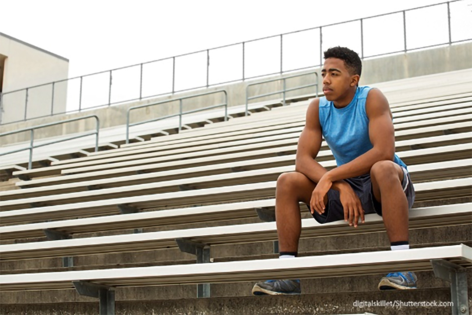 Stock photo of a male teenager sitting alone in a stadium’s bleachers