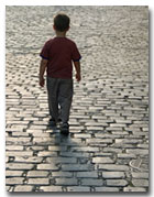 Young boy walking down a cobblestone street.