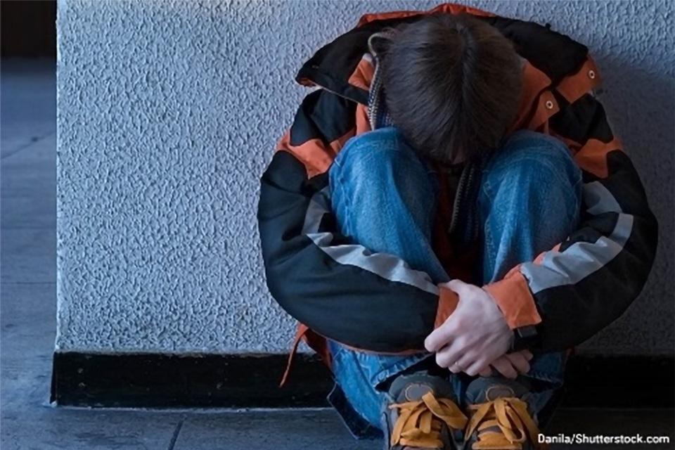 Stock photo of a youth sitting on the ground with his head tucked into his knees